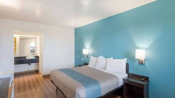 Une chambre d’hôtel comprenant un lit, des tables de chevet, une commode, un miroir et une salle de bain avec un lavabo et un miroir.