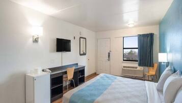 A hotel room with a bed, a desk, a chair, a television, a window with curtains, and a door.