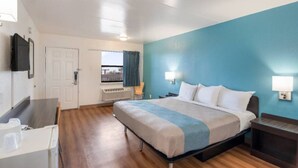 Una habitación de hotel con cama, mesitas de noche, un escritorio, una silla, una ventana con cortinas y un televisor en la pared.