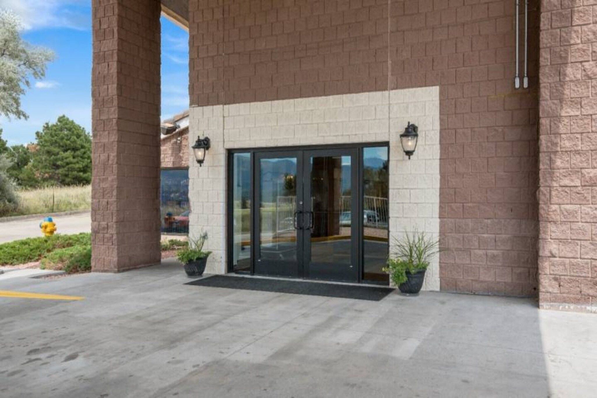 A building entrance with a glass door, potted plants, and a brick wall.
