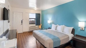 Een hotelkamer met een bed, een bureau, een stoel, een raam met gordijnen en een aan de muur bevestigde televisie.