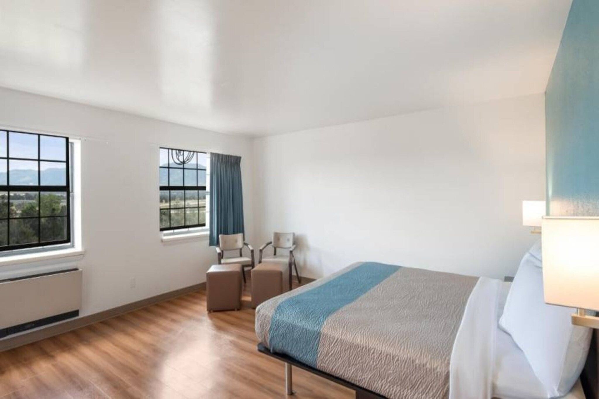 A hotel room with a bed, a desk, two chairs, a window with a view, and a radiator.