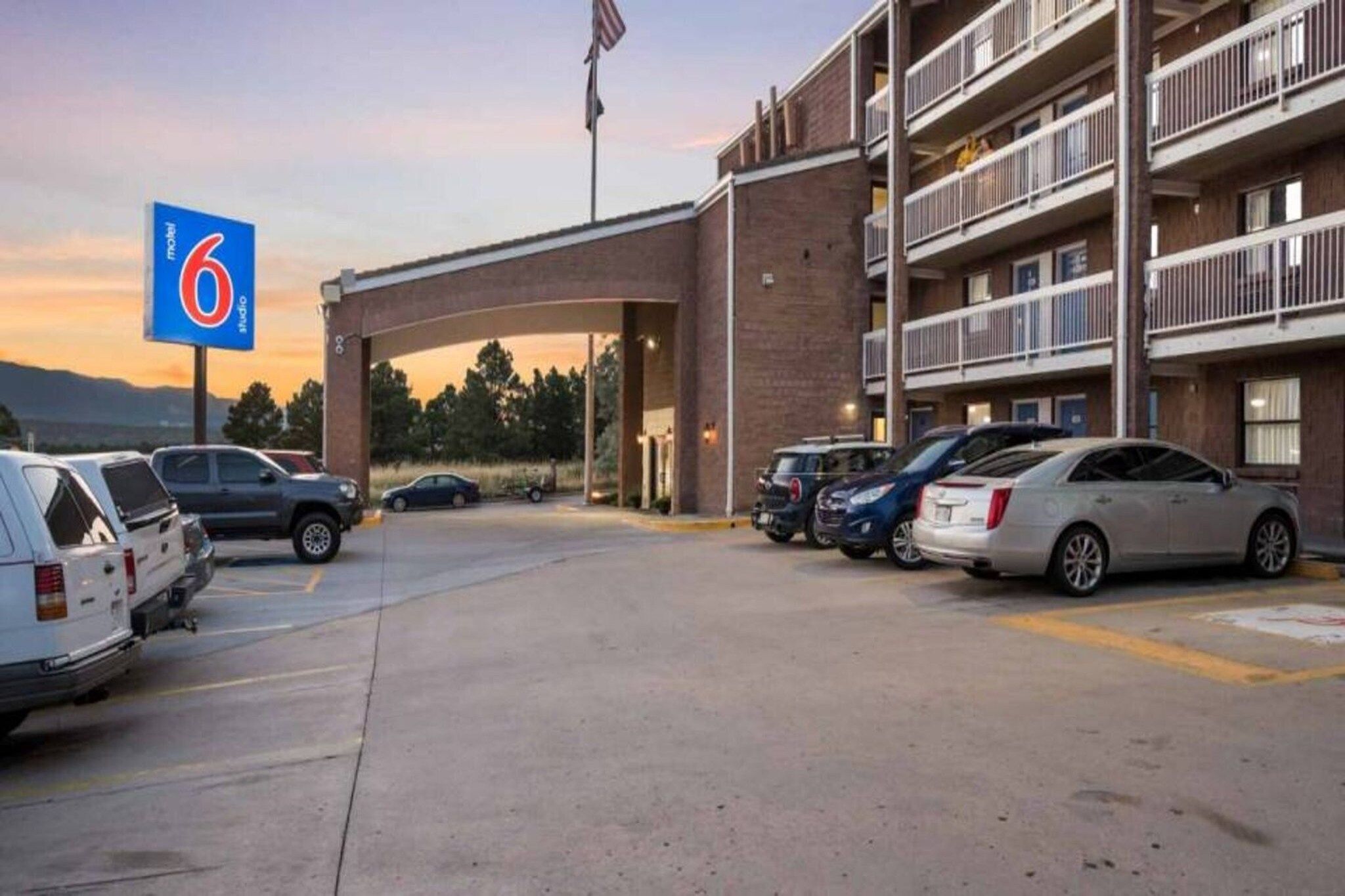 A motel with a parking lot, a brick building, and a sign indicating the number 6.