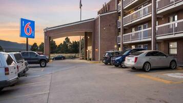 A motel with a parking lot, a brick building, and a sign indicating the number 6.