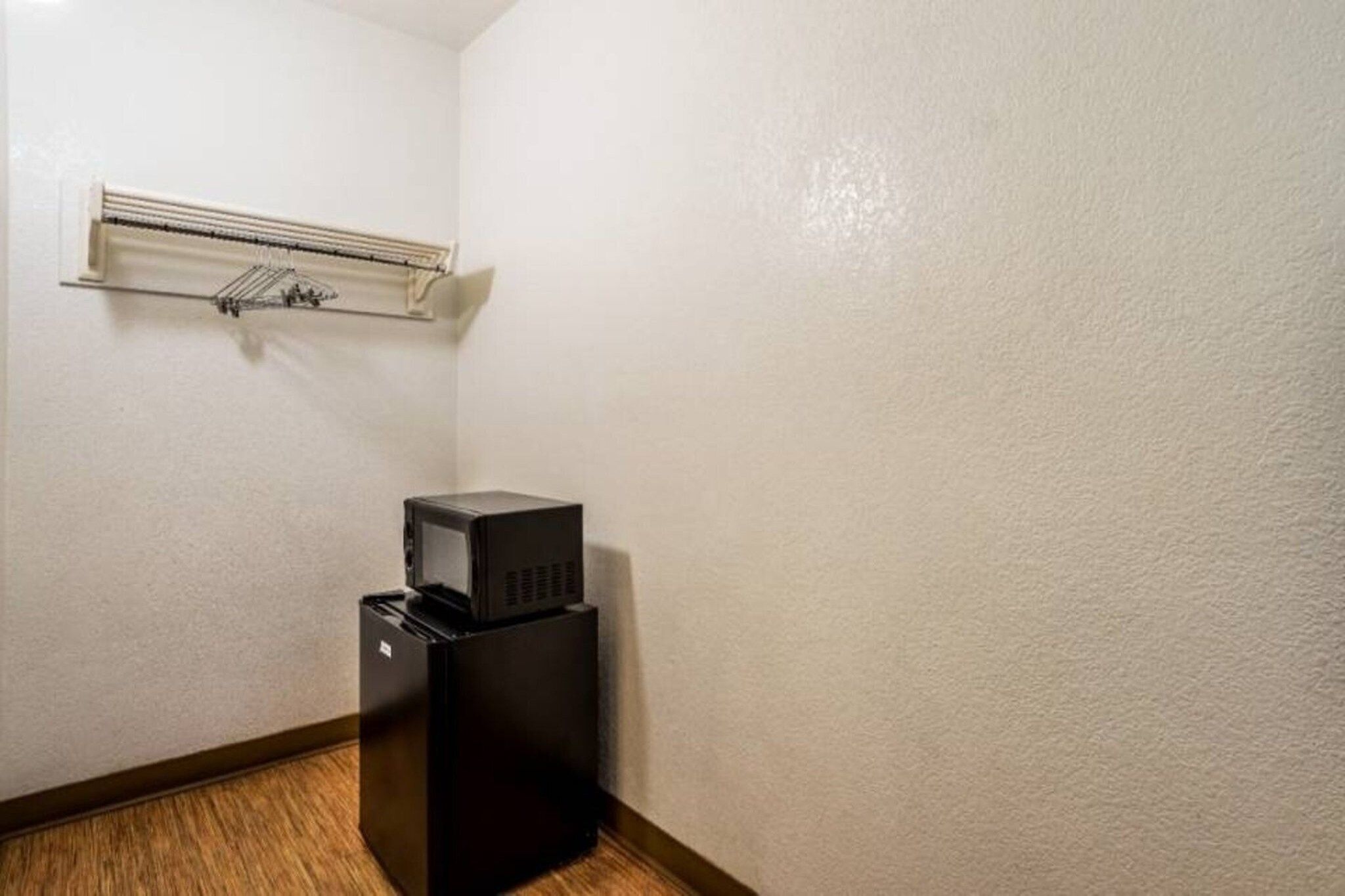 A corner room with a white textured wall, a black refrigerator, and a white ceiling-mounted air conditioning unit.