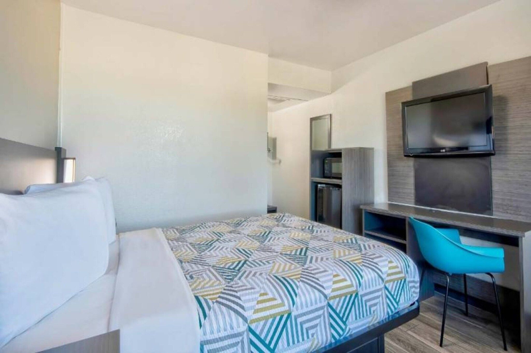 A hotel room with a bed, a desk, a chair, a television, and a microwave.