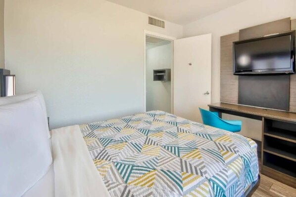 A hotel room with a bed, a TV mounted on the wall, and a small seating area.