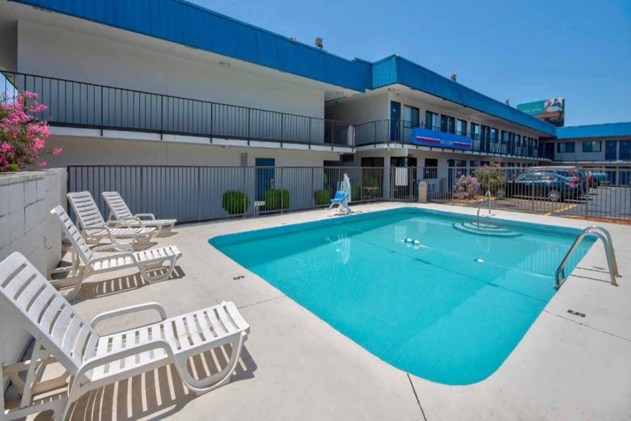 Une piscine avec des chaises longues, un bâtiment doté d’un toit bleu et un ciel dégagé.