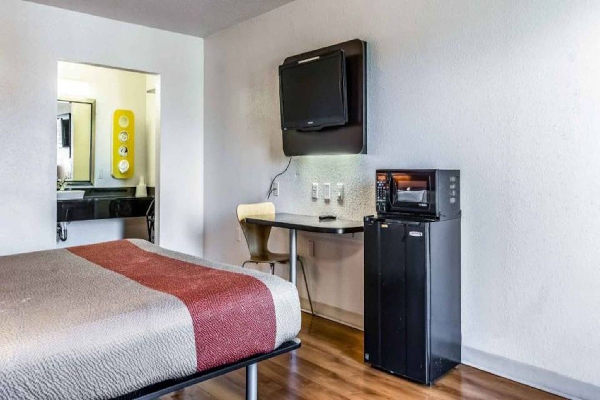 A hotel room with a bed, a desk with a computer, a TV, and a refrigerator.