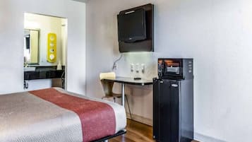 A hotel room with a bed, a desk with a computer, a TV, and a refrigerator.