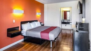 Habitación de hotel con cama, mesitas de noche, televisor y baño visible a través de una puerta abierta.