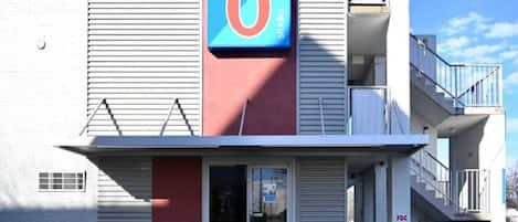 Un motel con un letrero grande con el número 6, una entrada principal con puerta de cristal y una escalera que sube a un nivel superior.