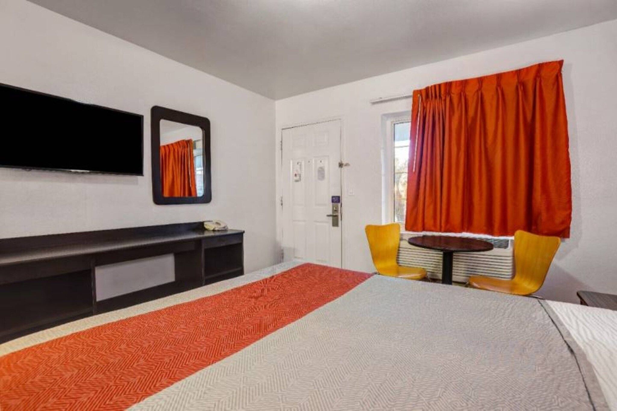 A hotel room with a bed, a desk, a chair, a television, and a door.