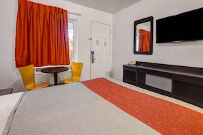 A hotel room with a bed, a small table, two chairs, a TV, and a door.