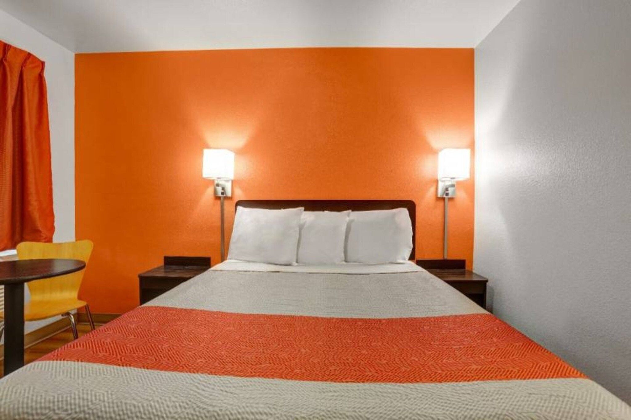 A hotel room with a bed, two bedside lamps, a chair, and a small table.