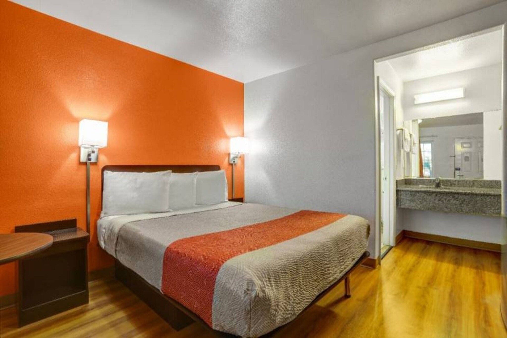 A hotel room with a bed, bedside tables, a mirror, and a wooden floor.