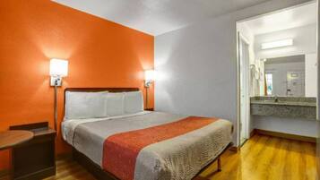A hotel room with a bed, bedside tables, a mirror, and a wooden floor.