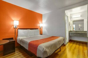 A hotel room with a bed, bedside tables, a mirror, and a wooden floor.