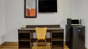 A room with a desk, a chair, a flat-screen TV, and a black refrigerator.