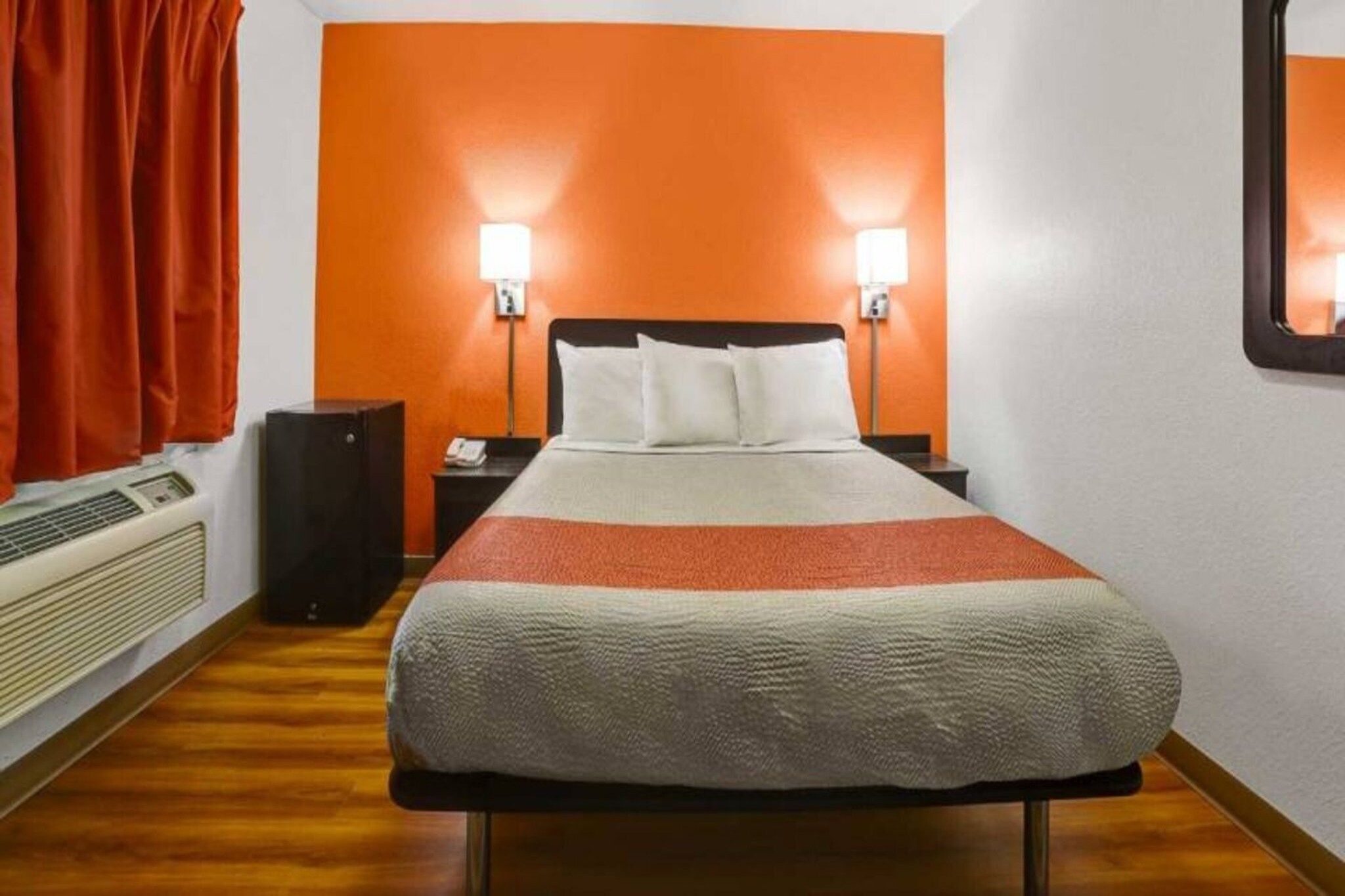 A hotel room with a bed, two bedside lamps, a telephone, a speaker, and a heater.
