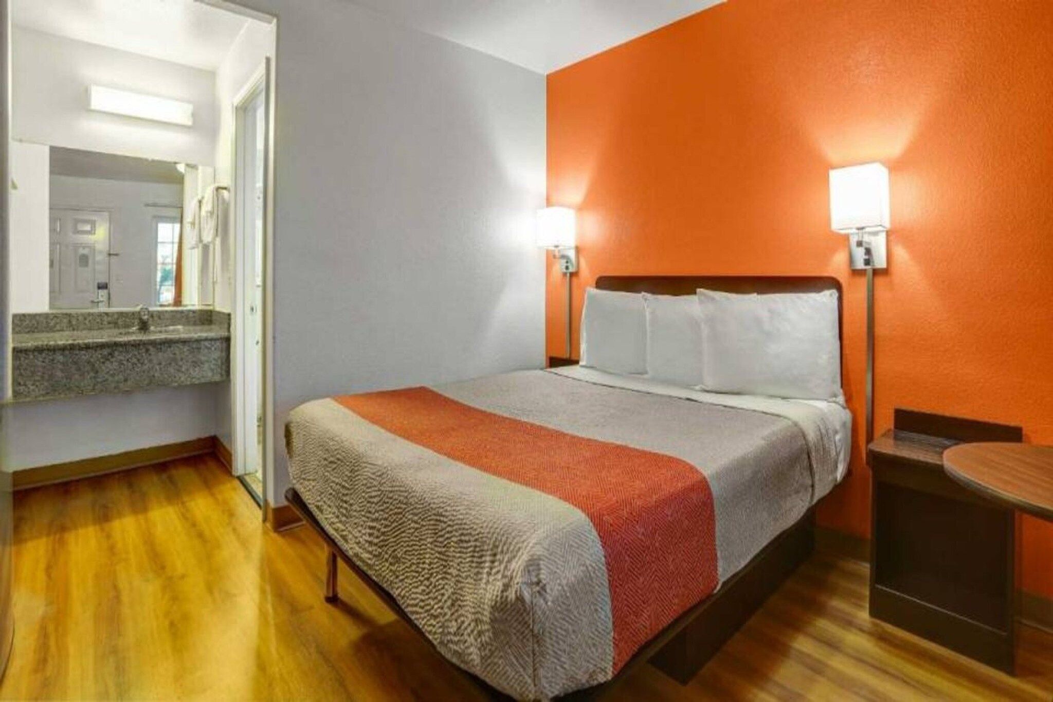 A hotel room with a bed, a nightstand, a mirror, and a wooden floor.