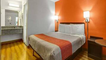A hotel room with a bed, a nightstand, a mirror, and a wooden floor.