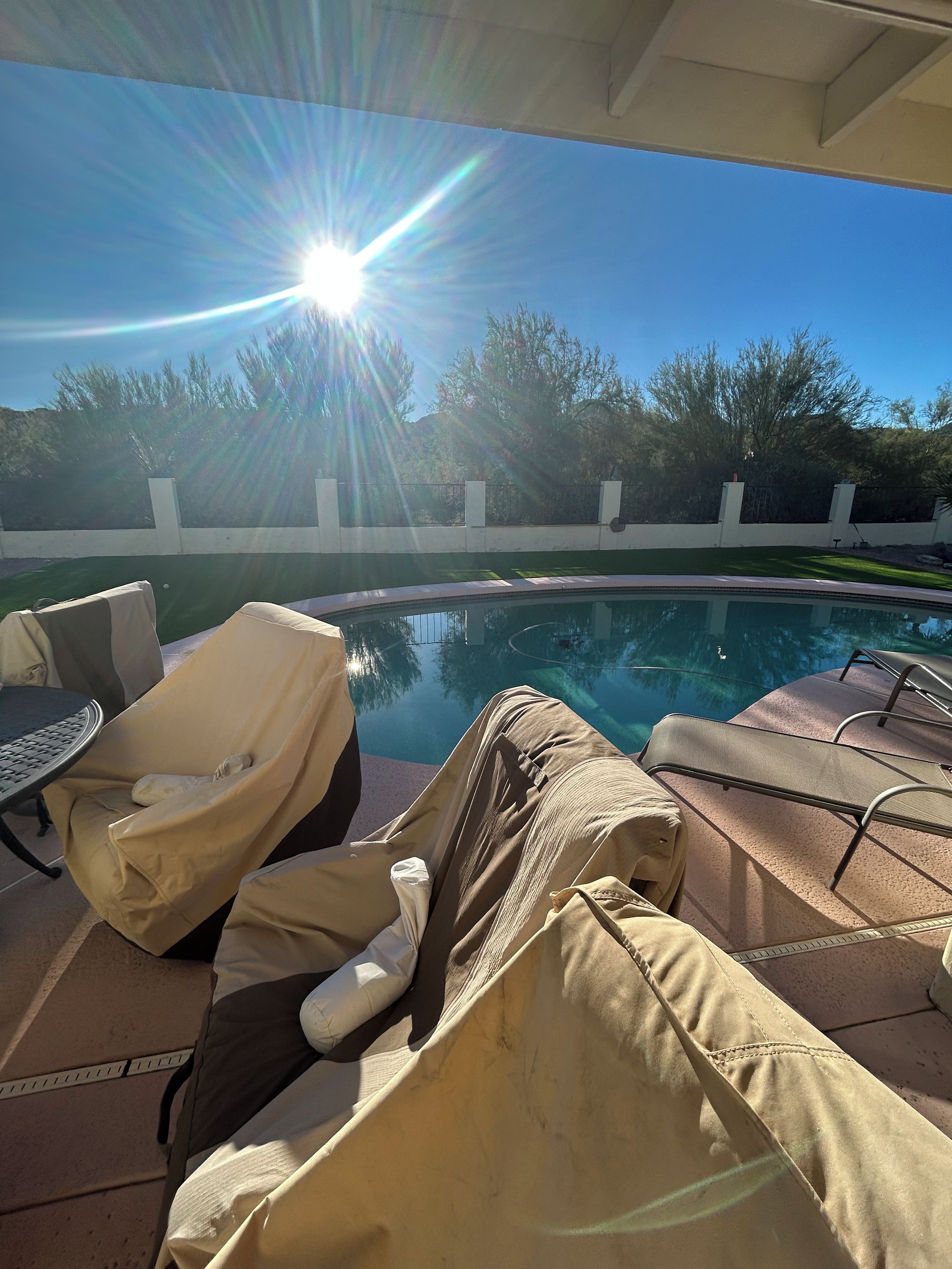 Un espace aménagé au bord de la piscine, avec des chaises longues et une table, entouré d’un petit muret et d’arbres.