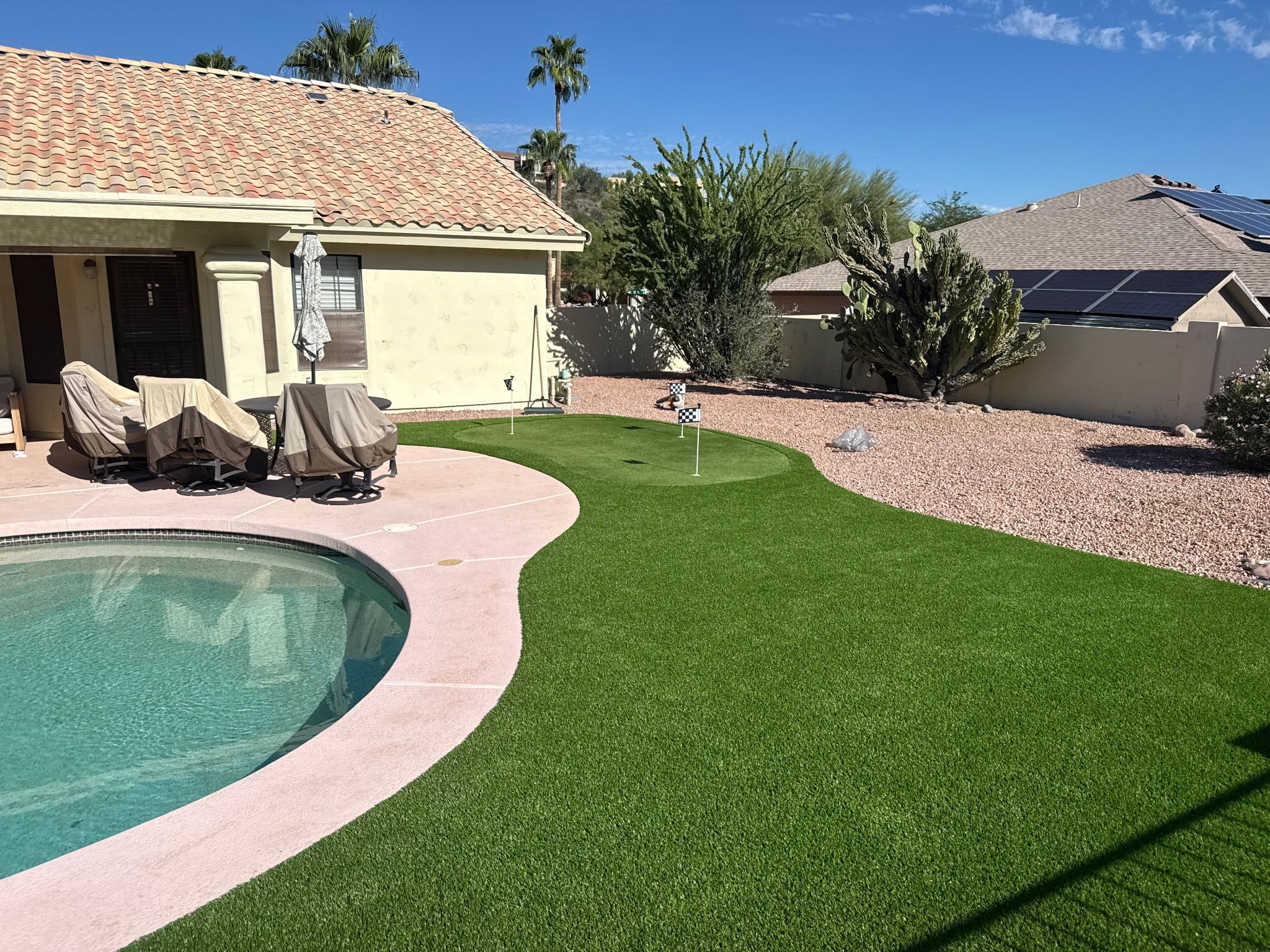 A pool area with artificial grass, a covered seating area, and a house with a tiled roof.
