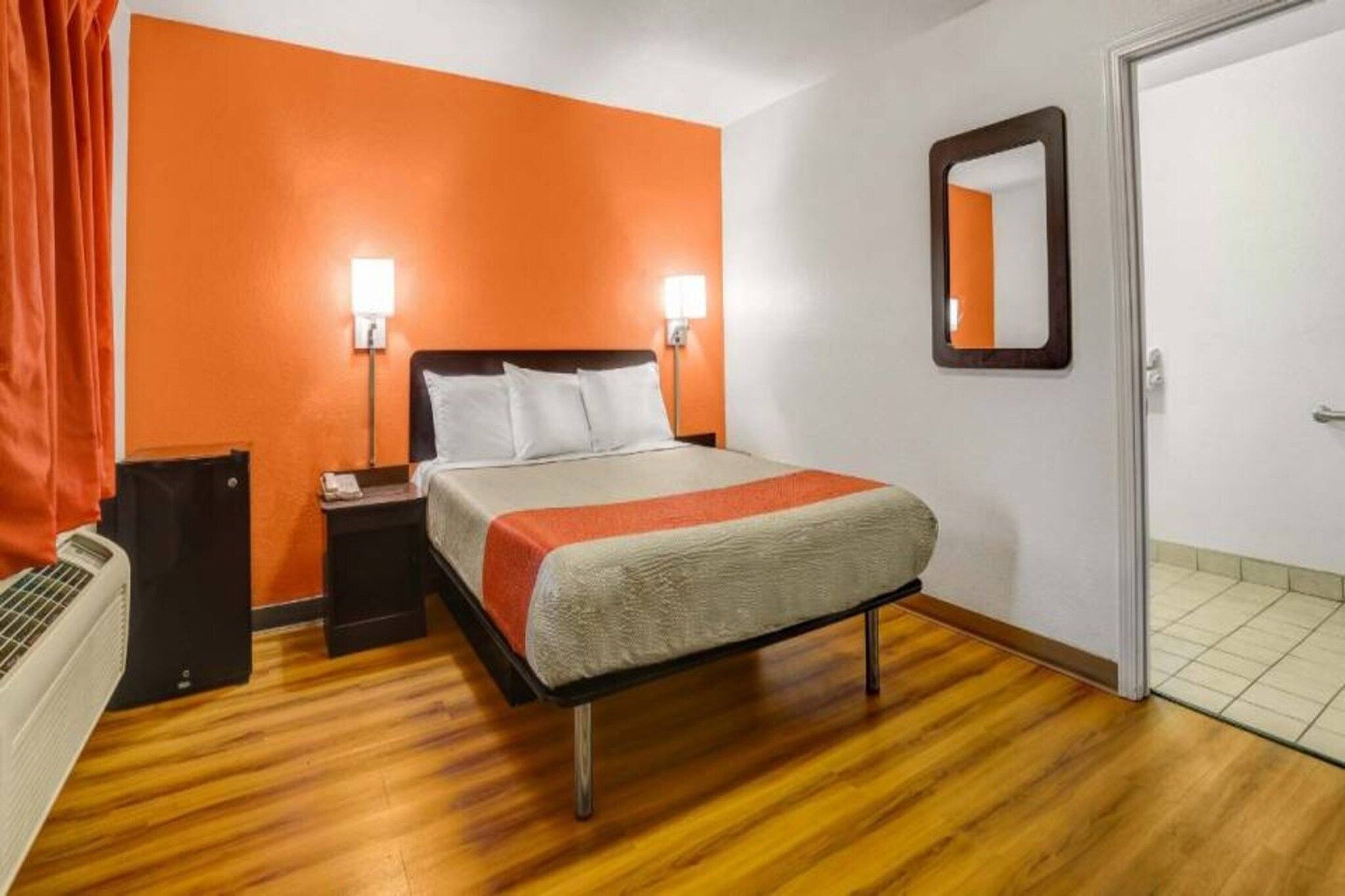 A hotel room with a bed, nightstand, lamp, and a door.