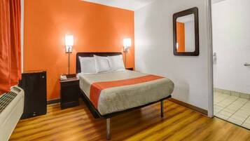 A hotel room with a bed, nightstand, lamp, and a door.