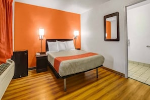 A hotel room with a bed, nightstand, lamp, and a door.