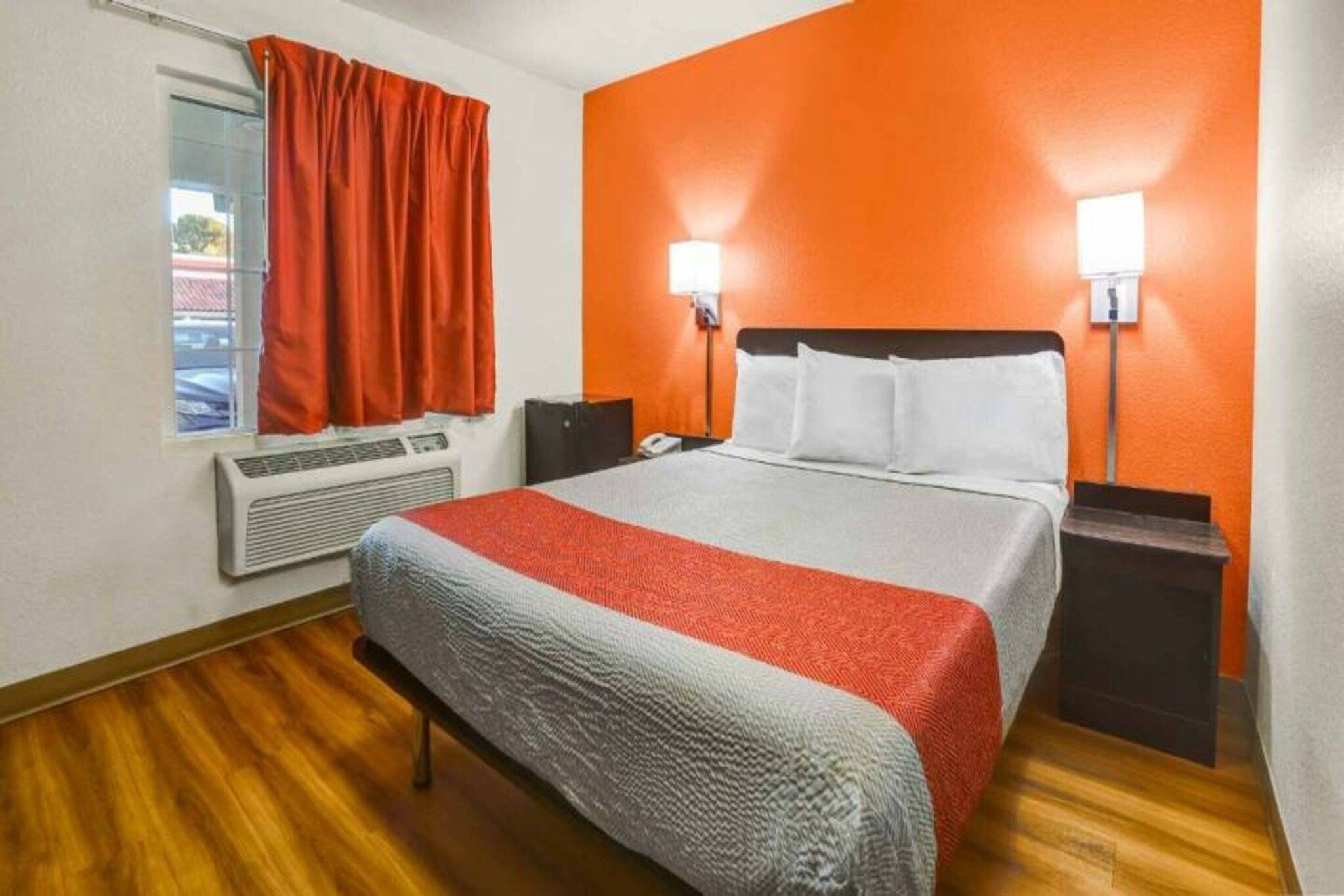 Une chambre d’hôtel équipée d’un lit, d’un climatiseur, d’une fenêtre avec des rideaux et de deux lampes fixées au mur.