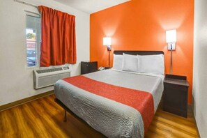 Een hotelkamer met een bed, een airconditioner, een raam met gordijnen en twee wandlampen.