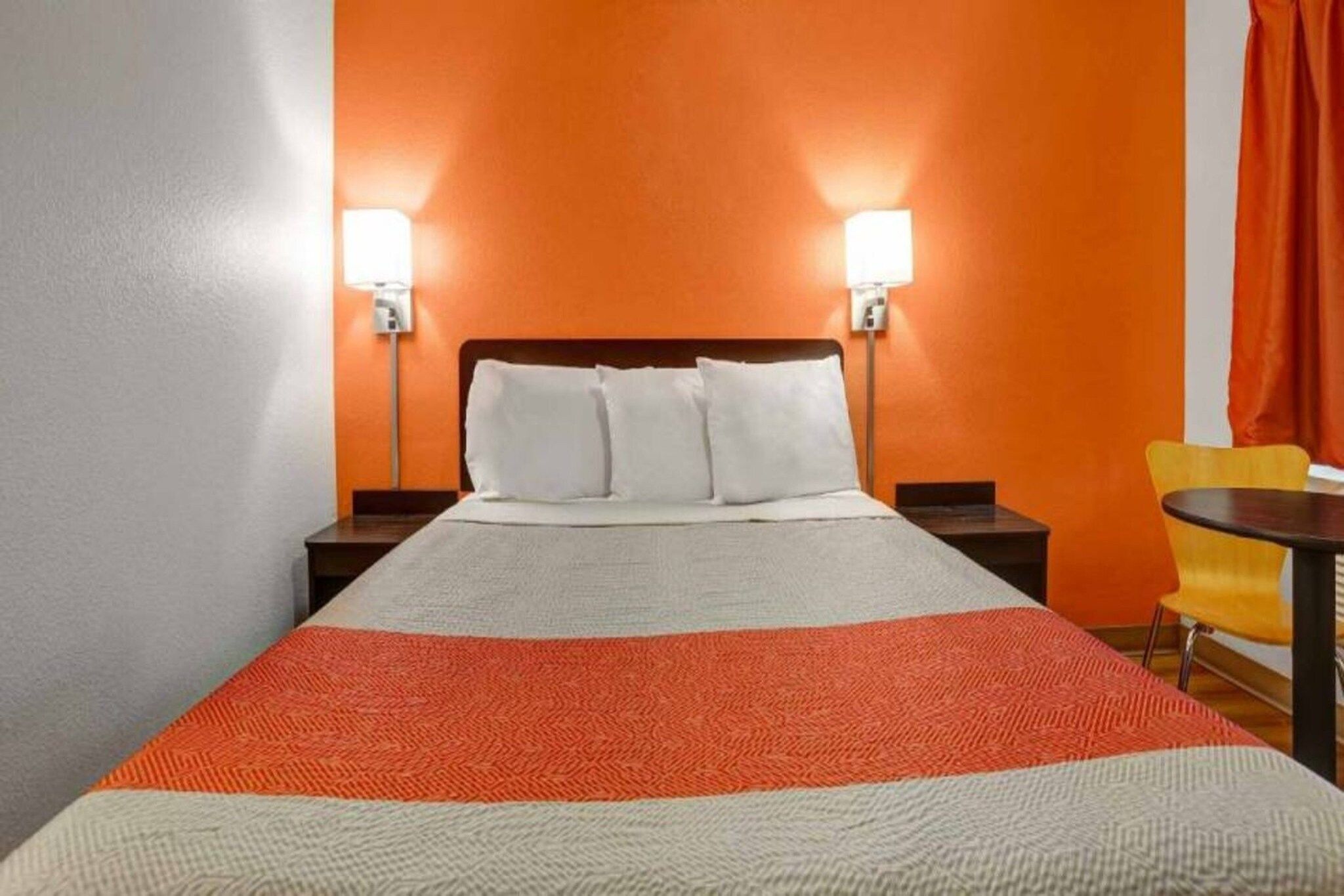 A hotel room with a bed, two bedside lamps, a chair, and a table.