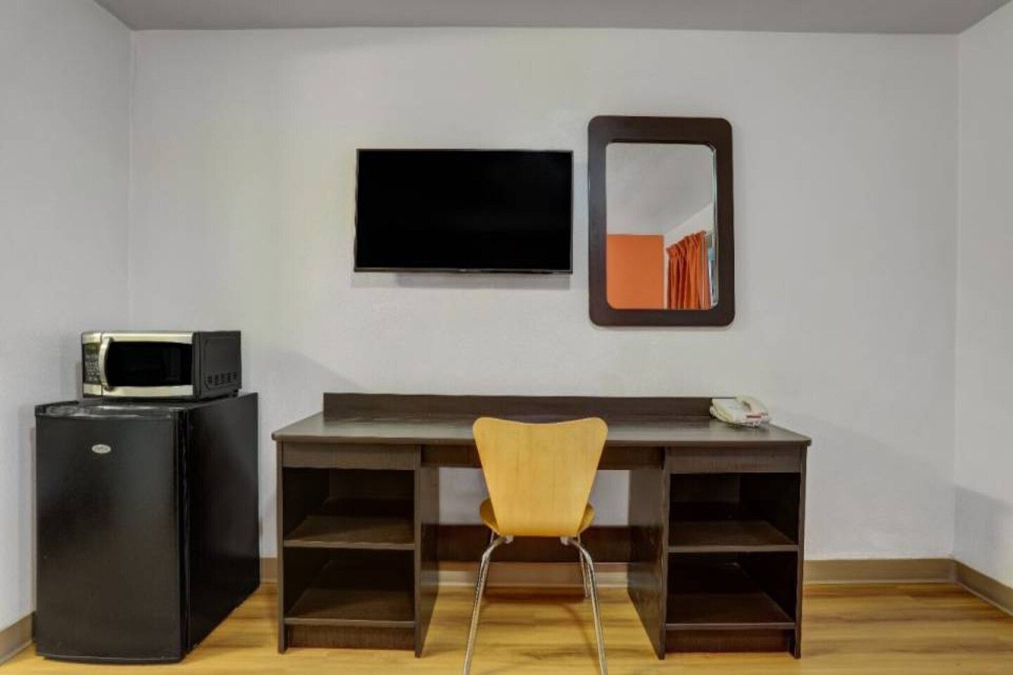 A room with a desk, a chair, a television, and a refrigerator.