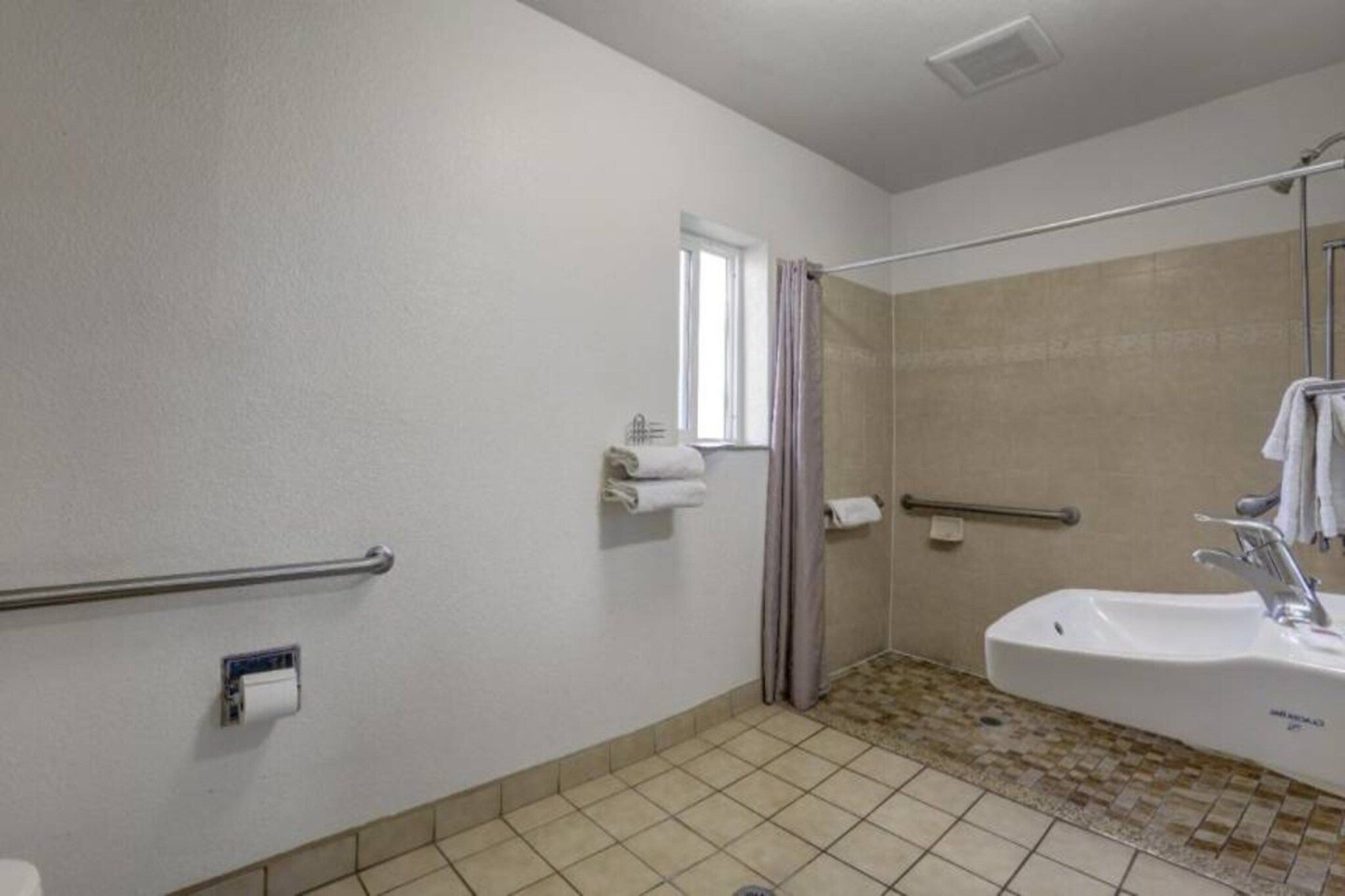 A bathroom with a bathtub, a shower, a handrail, a window, and a toilet.