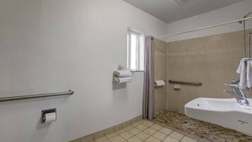 A bathroom with a bathtub, a shower, a handrail, a window, and a toilet.
