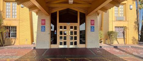 A building entrance with a covered porch, a brick facade, and a tiled ground.