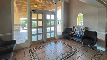 A reception area with a tiled floor, two black chairs, a wall-mounted display of brochures, and a large glass door leading outside.