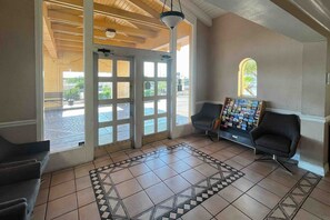 A reception area with a tiled floor, two black chairs, a wall-mounted display of brochures, and a large glass door leading outside. - 2 Queen Beds | Non-Smoking (Phoenix)