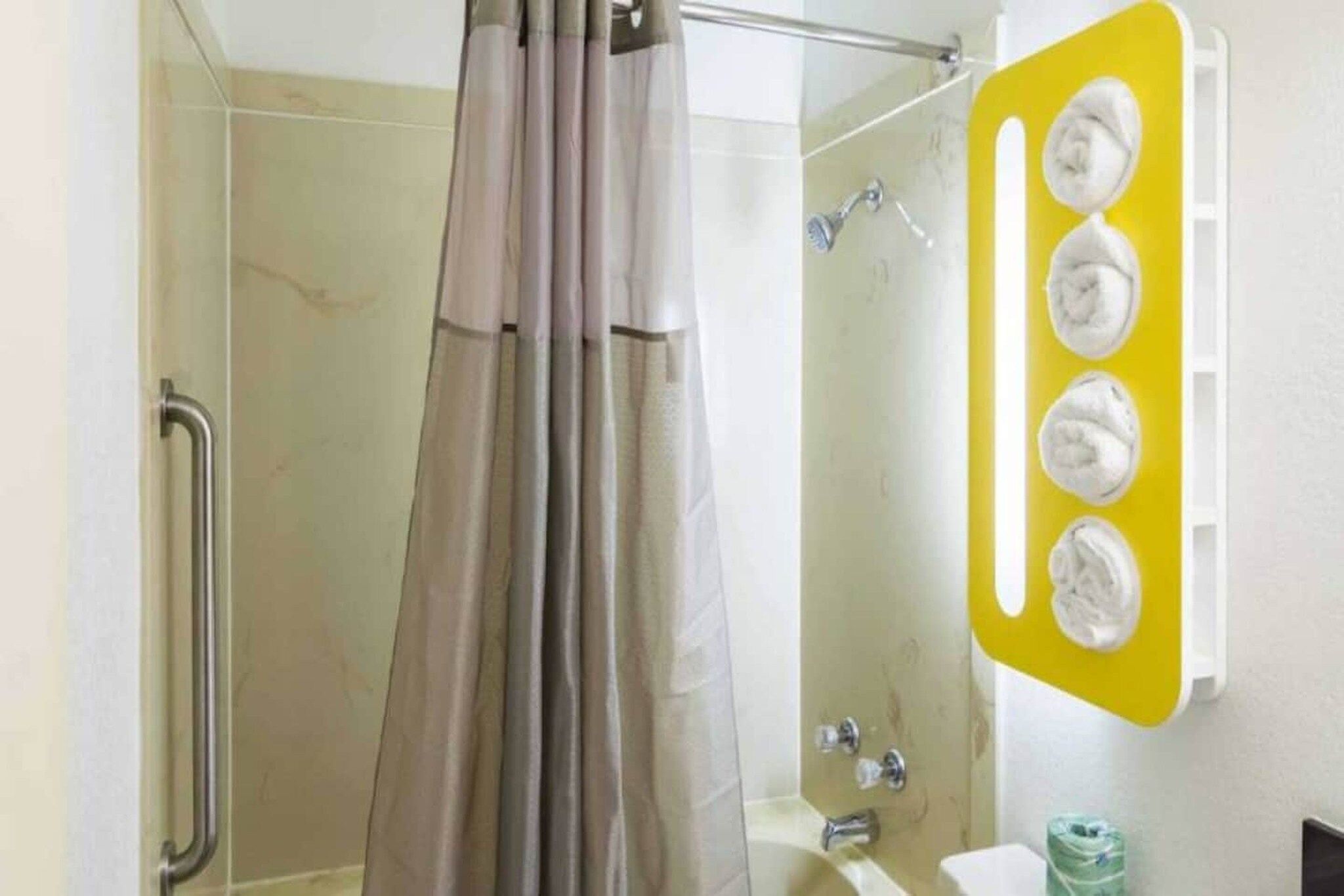Área de chuveiro com porta de vidro, chuveiro e porta-toalhas amarelo com várias toalhas.