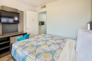 Hotellihuone, jossa on sänky, työpöytä tuolilla, televisio ja vaatekaappi.