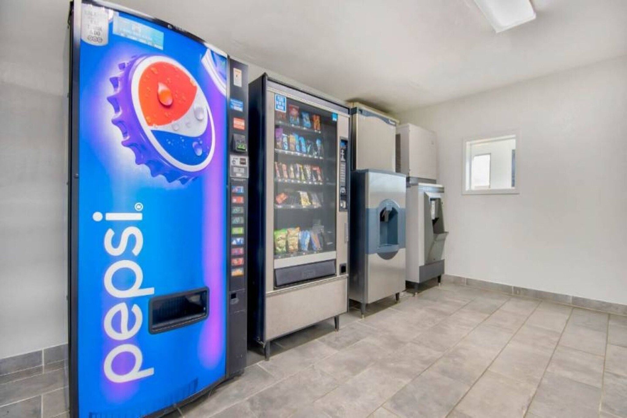 Et område med salgsautomater, inklusive en Pepsi-reklame, en snackautomat og en vanddåse-dispenser.