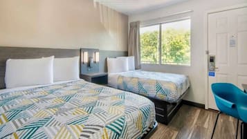 Habitación de hotel con dos camas, un escritorio, una silla, una ventana con vistas y una puerta.