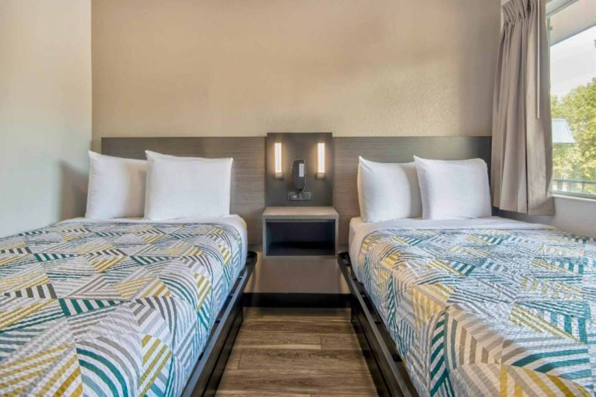 Habitació d'hotel amb dos llits, una tauleta de nit i una làmpada fixada a la paret.