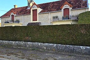 En bygning med en stenfassade, rødt tegltag og en velplejet hæk foran.
