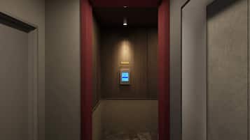 A narrow hallway with a wooden wall and a red accent wall. A digital elevator control panel is visible at the end of the hallway.