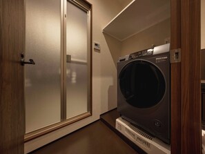A laundry room with a front-loading washing machine, a door with a handle, and a thermostat on the wall. - illi Vau Hamamatsucho (Minato-ku)