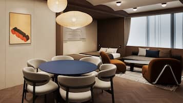 A modern hotel room with a round dining table, comfortable seating, a sofa, and a large window providing a view.