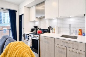 A modern kitchen with white cabinets, a stove, and a sink. - StayToronto -  Urban Serenity 1BR Suite - Downtown (Toronto)